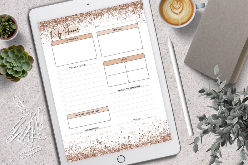 May include: A digital daily planner displayed on a tablet. The planner features sections for top priorities, schedule, meals, and notes, with a rose gold glitter design. A cup of coffee, a pen, and greenery are also visible.