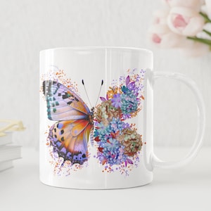 Puede incluir: Taza de cer&aacute;mica blanca con un dise&ntilde;o de mariposa y flores de colores. La mariposa tiene alas naranjas, moradas y azules. Las flores son moradas, azules y naranjas.