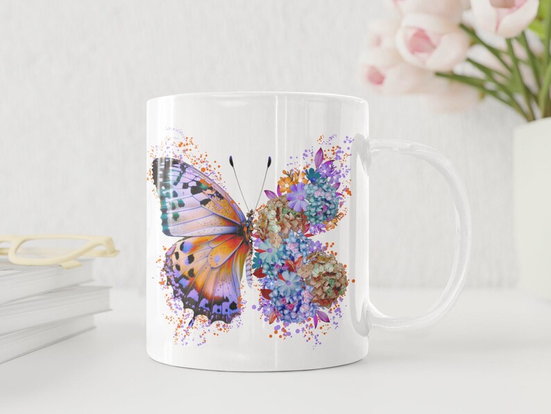 Puede incluir: Taza de cer&aacute;mica blanca con un dise&ntilde;o de mariposa y flores de colores. La mariposa tiene alas naranjas, moradas y azules. Las flores son moradas, azules y naranjas.