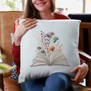 Pu&ograve; includere: Un cuscino azzurro chiaro con un'illustrazione ad acquerello di un libro aperto con fiori colorati che crescono dalle pagine.