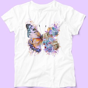 Puede incluir: Camiseta blanca con un dise&ntilde;o de mariposa colorida. La mariposa est&aacute; hecha de flores de acuarela p&uacute;rpura, azul, naranja y amarilla.