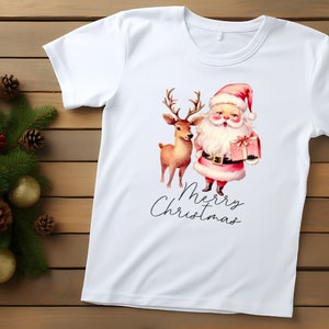 May include: White t-shirt featuring a watercolor illustration of Santa Claus holding a gift box and a reindeer. The words "Merry Christmas" are written in a script font below the image. The shirt is on a wooden surface.