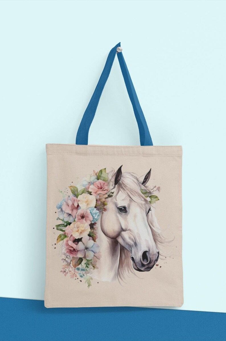 May include: A beige canvas tote bag with blue handles features a watercolor illustration of a white horse with a floral crown. The horse's head is facing the right side of the bag.