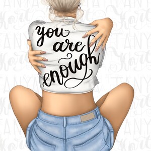 K&ouml;nnte beinhalten: Eine Frau tr&auml;gt ein wei&szlig;es Shirt mit dem Text "you are enough" in Schwarz. Sie tr&auml;gt Jeans-Shorts und hat ihre Arme um sich selbst geschlungen.
