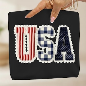 May include: Black tote bag with the word "USA" appliqued on the front. The letters are in red and white stripes, blue and white gingham, and navy blue with white polka dots, all trimmed with white lace.