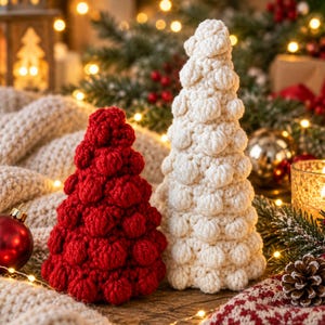 May include: Two cone-shaped decorative trees made of textured crochet yarn. One tree is a deep red color and the other is a cream white color. Both trees feature a repeating bobble stitch pattern that creates a bumpy, three-dimensional surface.