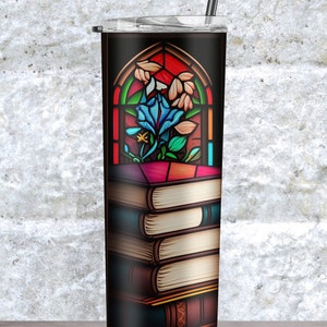 Peut inclure: Un gobelet en acier inoxydable avec un fond noir et un motif de vitrail repr&eacute;sentant une fleur bleue dans une fen&ecirc;tre. Le gobelet est surmont&eacute; d'une pile de livres.