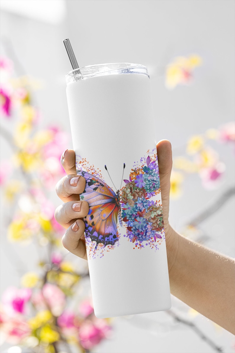 Puede incluir: Un vaso de acero inoxidable blanco con un dise&ntilde;o de mariposa y flores de colores. El vaso tiene una tapa y una pajita.