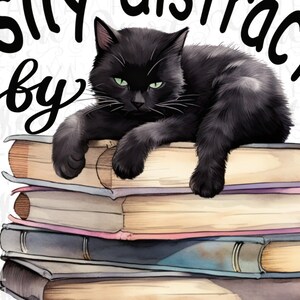 May include: A black cat with green eyes is lying on a stack of books. The text "easily distracted by" is written above the cat and the text "books" is written below the cat.