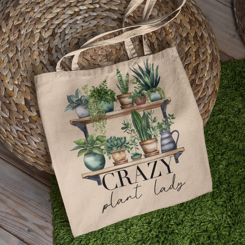 May include: A beige canvas tote bag with a design of potted plants on shelves and the text "CRAZY plant lady".