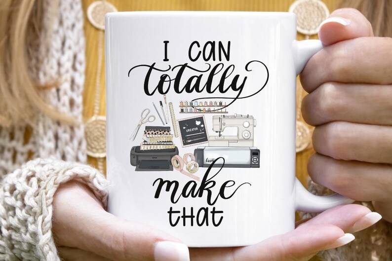 Może przedstawiać: Biały kubek ceramiczny z napisem "I can totally make that" w czarnym, ozdobnym pismie. Kubek zawiera grafikę z r&oacute;żnymi przyborami do rękodzieła, w tym maszyną do szycia, nożyczkami, nicią i drukarką.
