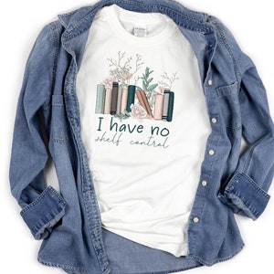 May include: White t-shirt with a graphic of a stack of books with flowers and the text "I have no shelf control".