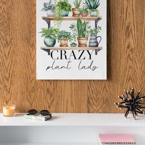May include: A white canvas print with a watercolor illustration of a shelf with potted plants. The text "CRAZY plant lady" is written below the shelf.