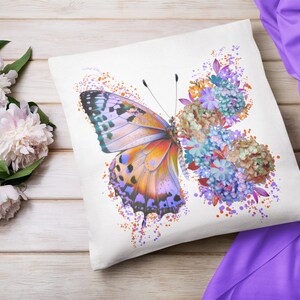 Puede incluir: Una almohada blanca con una mariposa colorida y un dise&ntilde;o floral. La mariposa es naranja, morada y azul con marcas negras. Las flores son azules, moradas y naranjas.