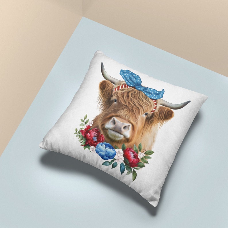 Op de afbeelding: Vierkantig wit kussen met een Schotse hooglander met een blauwe strik en een rood-wit gestreepte hoofdband. De koe is omgeven door rode, blauwe en witte bloemaccenten. Het kussen heeft een lichtblauwe en beige achtergrond.