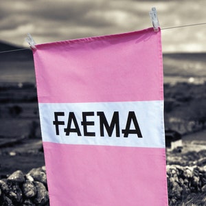 May include: A pink fabric banner with a white stripe and the word "FAEMA" printed in black letters.