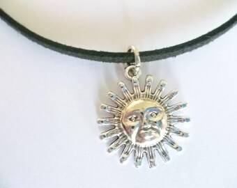 May include: A black leather choker necklace with a silver sun pendant. The sun has a face with a serious expression.