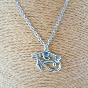 May include: Silver-toned necklace featuring an Eye of Horus pendant. The pendant is a stylized eye with intricate details, suspended from a delicate chain. The necklace is displayed against a neutral background.