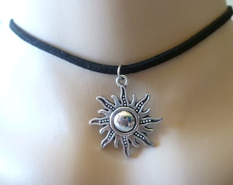 May include: A black suede choker necklace with a silver sun pendant. The sun has a detailed design with rays and a round center.