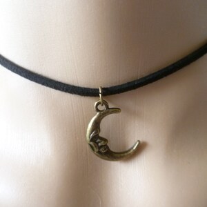 Puede incluir: Un collar gargantilla de ante negro con un colgante de media luna dorado.