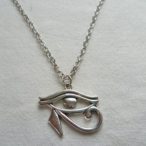 May include: Silver-toned necklace featuring an Eye of Horus pendant. The pendant is a stylized eye with intricate details, suspended from a delicate chain. The necklace is likely made of a metal alloy and is suitable for everyday wear. The design is inspired by ancient Egyptian symbolism.