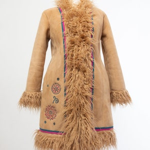 May include: A long brown suede coat with a faux fur collar and trim. The coat has a colorful embroidered design on the front and a pink and teal stripe down the front.