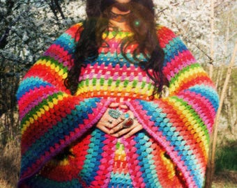 May include: A vibrant, rainbow-colored crochet dress with long, flared sleeves. The dress features a spectrum of colors, including red, orange, yellow, green, blue, and purple. The handmade garment has a unique, bohemian style, perfect for a festival or a casual outing.