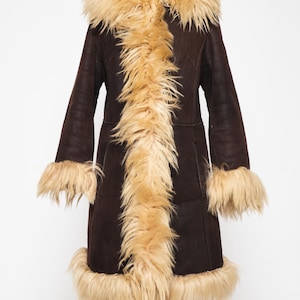 Authentic vintage Penny Lane coat in genuine sheepskin with shearling fur trim. Women's 70s Afghan coat inspired by Woodstock fashion and classic boho winter style..May include: A dark brown coat with a tan faux fur collar, trim, and cuffs. The long coat is displayed on a mannequin and has a vintage, retro style. The coat is knee-length and has a button closure.