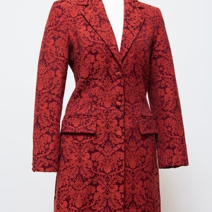May include: A long, red coat with a floral pattern. The coat has a notched collar, two front pockets, and a two-button closure. The coat is displayed on a mannequin.