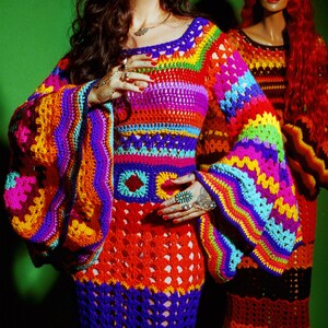 May include: A vibrant, handmade crochet dress in a rainbow of colors, including orange, purple, blue, and green. The dress features long, bell sleeves and a fitted bodice. A second dress in similar colors is visible in the background.