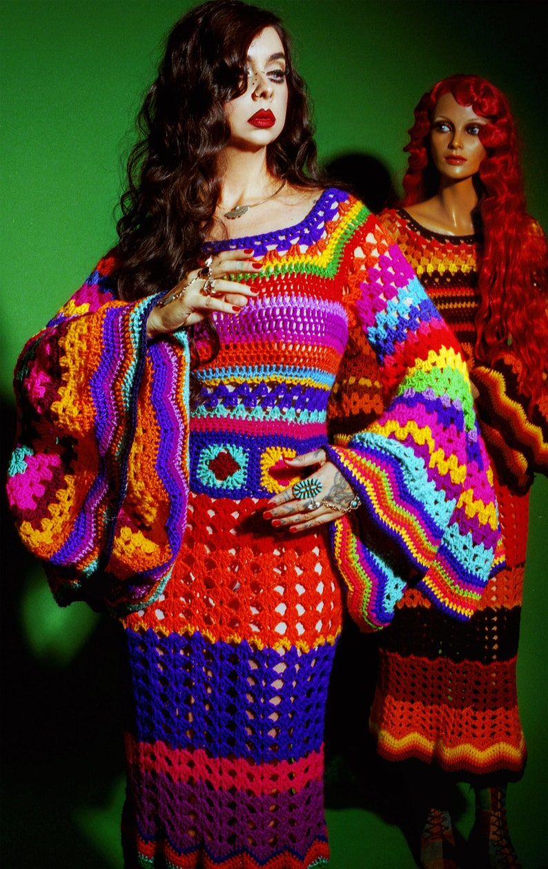May include: A vibrant, handmade crochet dress in a rainbow of colors, including orange, purple, blue, and green. The dress features long, bell sleeves and a fitted bodice. A second dress in similar colors is visible in the background.