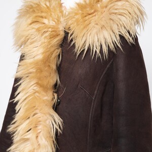 May include: A brown shearling coat with a tan faux fur collar and trim. The coat has a button closure and a classic design. The faux fur trim adds a touch of luxury and warmth. This coat is perfect for cold weather.
