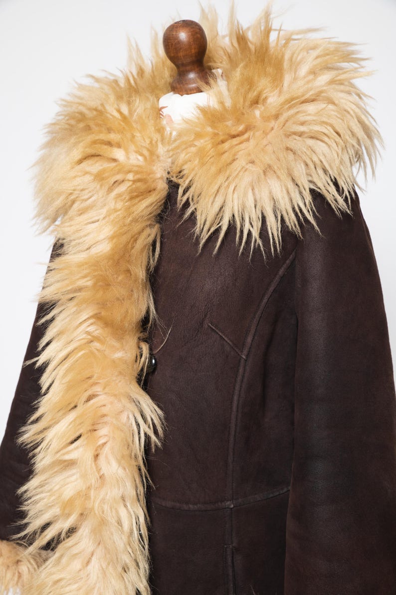 May include: A brown shearling coat with a tan faux fur collar and trim. The coat has a button closure and a classic design. The faux fur trim adds a touch of luxury and warmth. This coat is perfect for cold weather.