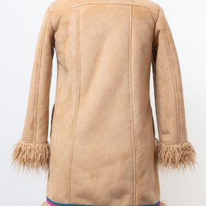 May include: A brown suede coat with a faux fur collar and trim. The coat has a long, fitted silhouette and a decorative trim around the bottom.