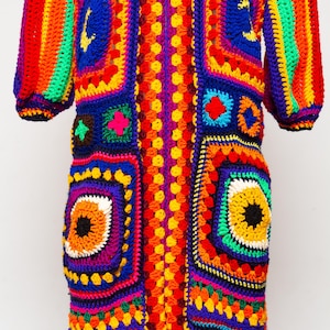 May include: A long, colorful crochet cardigan with a zipper closure. The cardigan is made of a variety of bright colors, including red, orange, yellow, green, blue, and purple. The cardigan has a geometric pattern and is crocheted in a granny square style.
