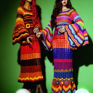 May include: Two mannequins display colorful, handmade crochet dresses against a green backdrop. One dress features orange, brown, and yellow hues, while the other showcases a rainbow of colors. Decorative spheres are in the foreground.