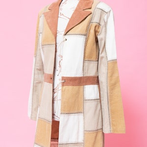 K&ouml;nnte beinhalten: Eine lange Patchworkjacke in Braun, Beige und Wei&szlig;. Die Jacke hat einen Kragen und einen Knopfverschluss. Sie ist aus Cord und hat ein gestepptes Design.