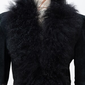 May include: Black suede jacket with a large, fluffy black fur collar. The jacket has long sleeves and a tailored fit, with decorative stitching on the cuffs. The jacket is displayed on a mannequin.