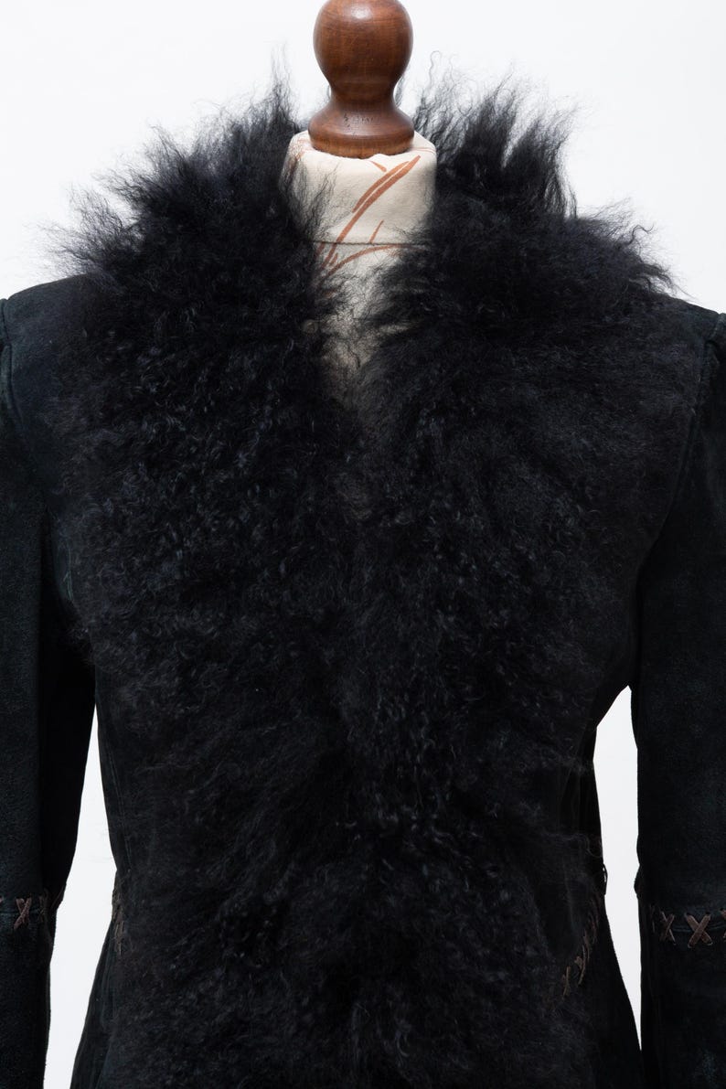 May include: Black suede jacket with a large, fluffy black fur collar. The jacket has long sleeves and a tailored fit, with decorative stitching on the cuffs. The jacket is displayed on a mannequin.