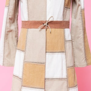 K&ouml;nnte beinhalten: Eine lang&auml;rmelige Patchwork-Jacke mit braunem Cordkragen und G&uuml;rtel. Die Jacke besteht aus verschiedenen Farbt&ouml;nen von beige und wei&szlig;em Cordstoff.