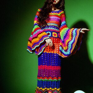 May include: A vibrant, handmade crochet dress in a rainbow of colors. The dress features long, flared sleeves and a fitted bodice that flows into a floor-length skirt. The intricate crochet work showcases a variety of patterns and textures, creating a bohemian aesthetic.