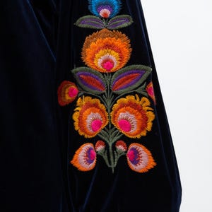 May include: Dark navy blue velvet fabric with a floral embroidery design. The embroidery features orange, pink, purple, and blue flowers with green leaves. The sleeve is gathered at the wrist.