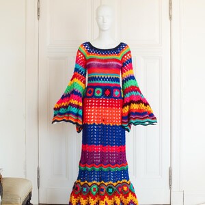 May include: A vibrant, handmade crochet dress in a rainbow of colors, including red, orange, blue, and green. The dress features a round neckline, long bell sleeves, and a flared skirt. It is displayed on a mannequin.