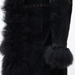 May include: Black suede coat with a fluffy, textured trim and cuffs. The coat features decorative brown stitching along the seams and edges. The coat is displayed on a wooden stand against a white background.