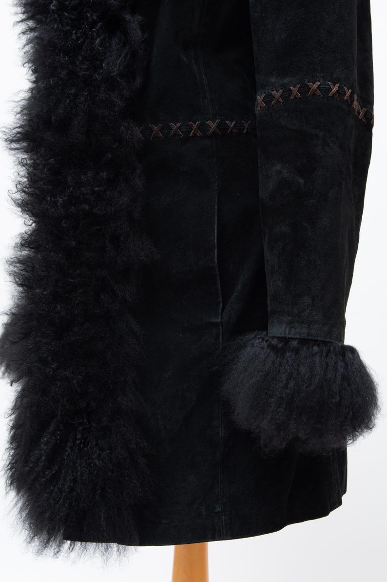 May include: Black suede coat with a fluffy, textured trim and cuffs. The coat features decorative brown stitching along the seams and edges. The coat is displayed on a wooden stand against a white background.