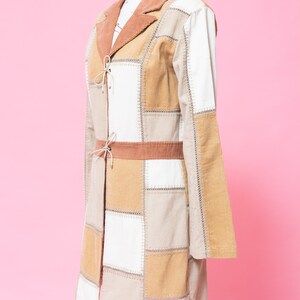 K&ouml;nnte beinhalten: Ein langer Patchwork-Mantel mit braunem Cordkragen und G&uuml;rtel. Der Mantel besteht aus verschiedenen Braunt&ouml;nen und wei&szlig;em Stoff und hat einen Bindeverschluss vorne.
