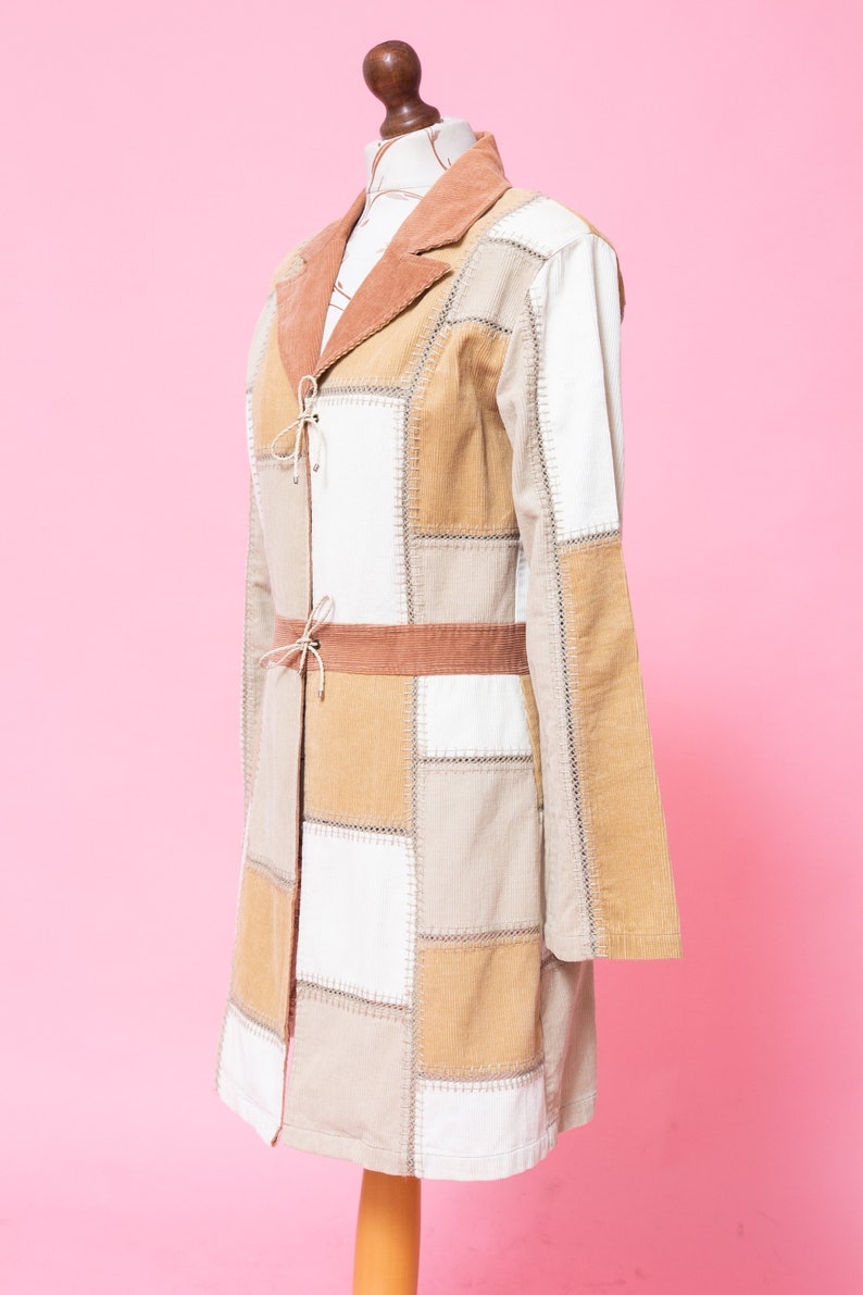 K&ouml;nnte beinhalten: Ein langer Patchwork-Mantel mit braunem Cordkragen und G&uuml;rtel. Der Mantel besteht aus verschiedenen Braunt&ouml;nen und wei&szlig;em Stoff und hat einen Bindeverschluss vorne.