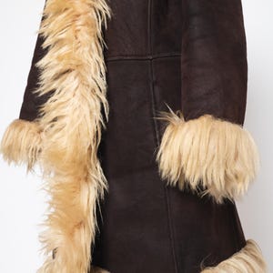 May include: A dark brown coat with tan faux fur trim along the collar, cuffs, and hem. The coat has a button closure and a classic design, suitable for cold weather. The faux fur adds a touch of luxury.