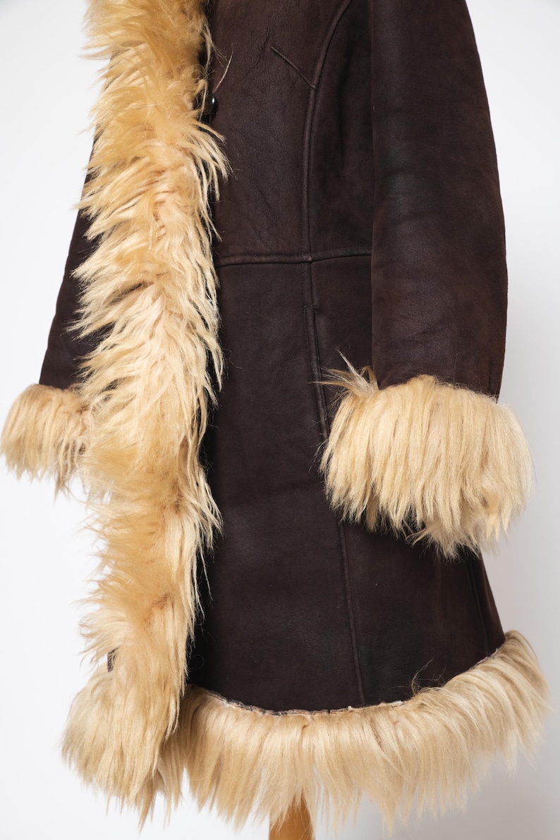May include: A dark brown coat with tan faux fur trim along the collar, cuffs, and hem. The coat has a button closure and a classic design, suitable for cold weather. The faux fur adds a touch of luxury.