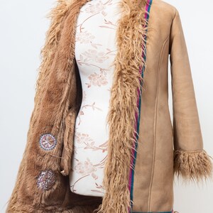 May include: A brown faux fur lined suede coat with a pink and teal trim. The coat has decorative embroidery on the front.